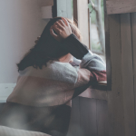 Photo of woman leaning on a window holding head with hands. By Dương Nhân - used by permission on Pexels.