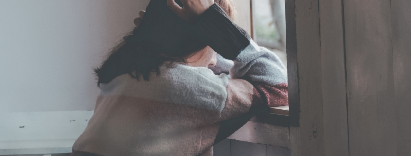 Photo of woman leaning on a window holding head with hands. By Dương Nhân - used by permission on Pexels.