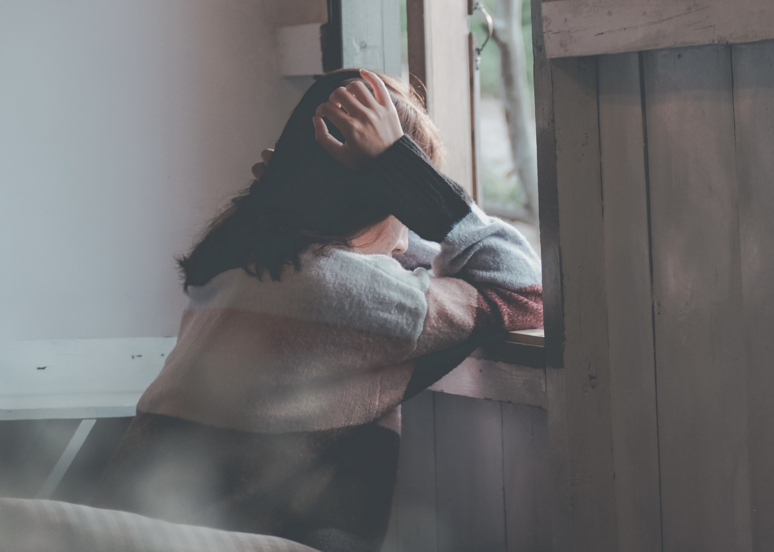 Photo of woman leaning on a window holding head with hands. By Dương Nhân - used by permission on Pexels.