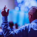 A man worshipping in a church with his hand held up.