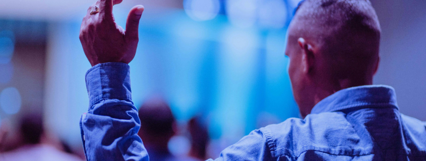 A man worshipping in a church with his hand held up.